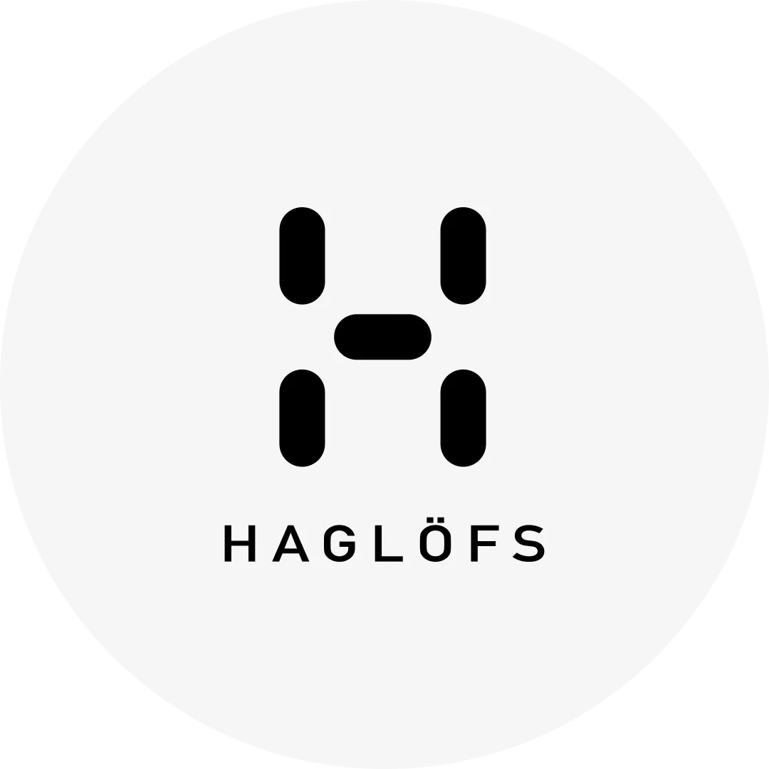 Svart stiliserat "H" med texten "Haglöfs" under, på vit cirkulär bakgrund.